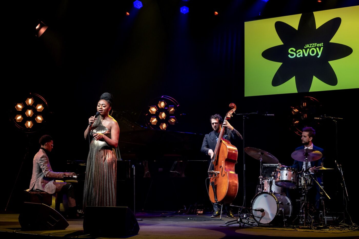 Samara Joy laulaa, bändi soittaa pianoa, bassoa ja rumpuja Savoy-teatterin lavalla. Taustalla Savoy JAZZFest logo.